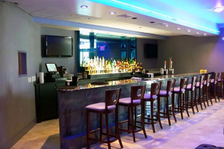 Restaurant bar with backlit liquor display and a row of upholstered bar stools