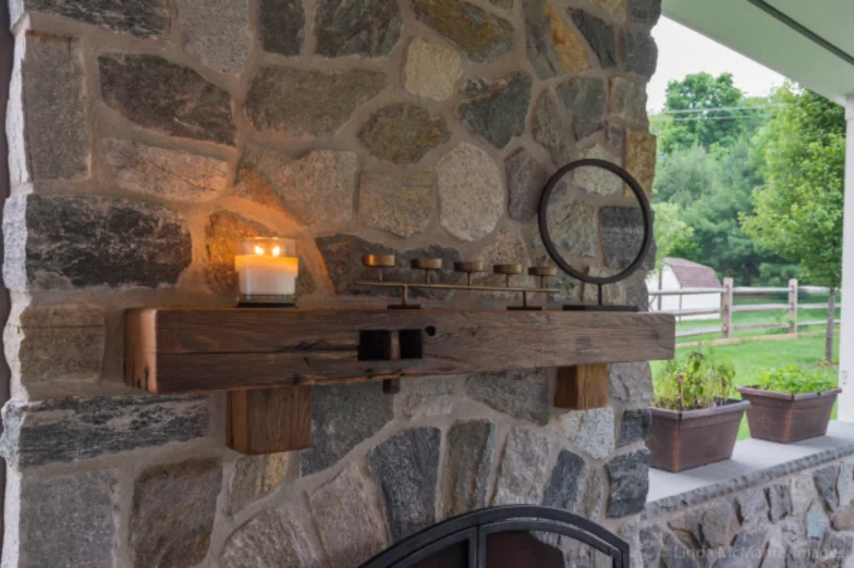 Detail of a fieldstone fireplace with a reclaimed timber mantel and candles